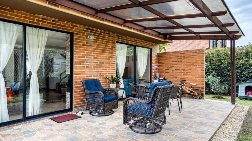 The Hoque Depot Outdoor area features wicker furniture with blue cushions under a transparent roof.